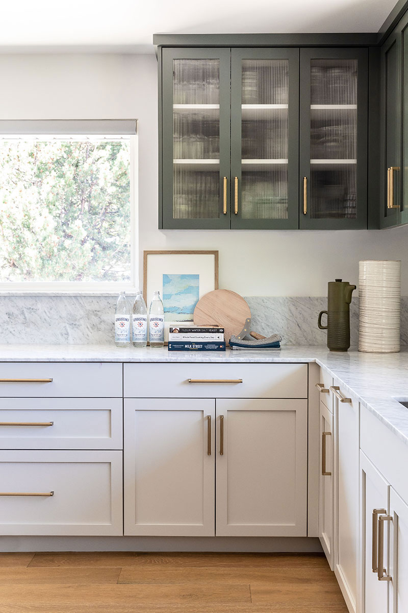 L shaped kitchen counter with marble like backsplash and matt green cupboards.